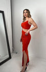 Woman in vibrant red crop top and ruched skirt set with side slit, posing in high heels