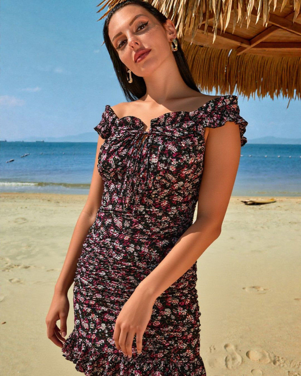 Woman wearing a floral ruffle dress on a tropical beach under a straw hut
