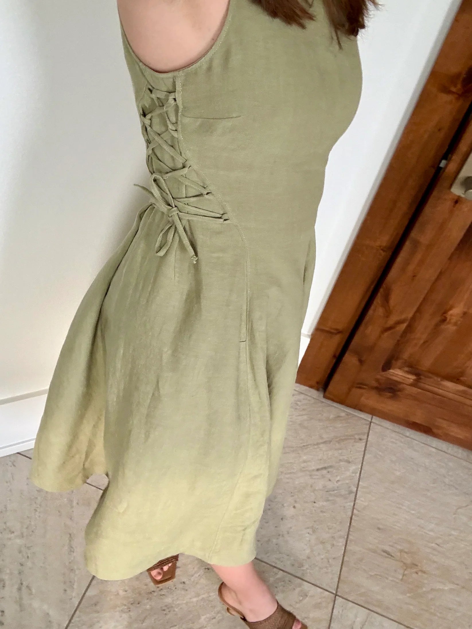 Lincoln Paris sage linen dress hanging on a wooden hanger, showcasing lightweight, breathable fabric and relaxed fit.