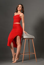 Woman in a red ruched two-piece outfit with spaghetti straps and high-slit skirt posing indoors