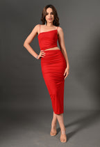 Woman in a fitted red ruched midi dress with spaghetti straps, standing against gray background