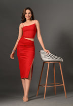 Woman in a red ruched midi skirt set with a slit, posing by a modern stool on gray backdrop