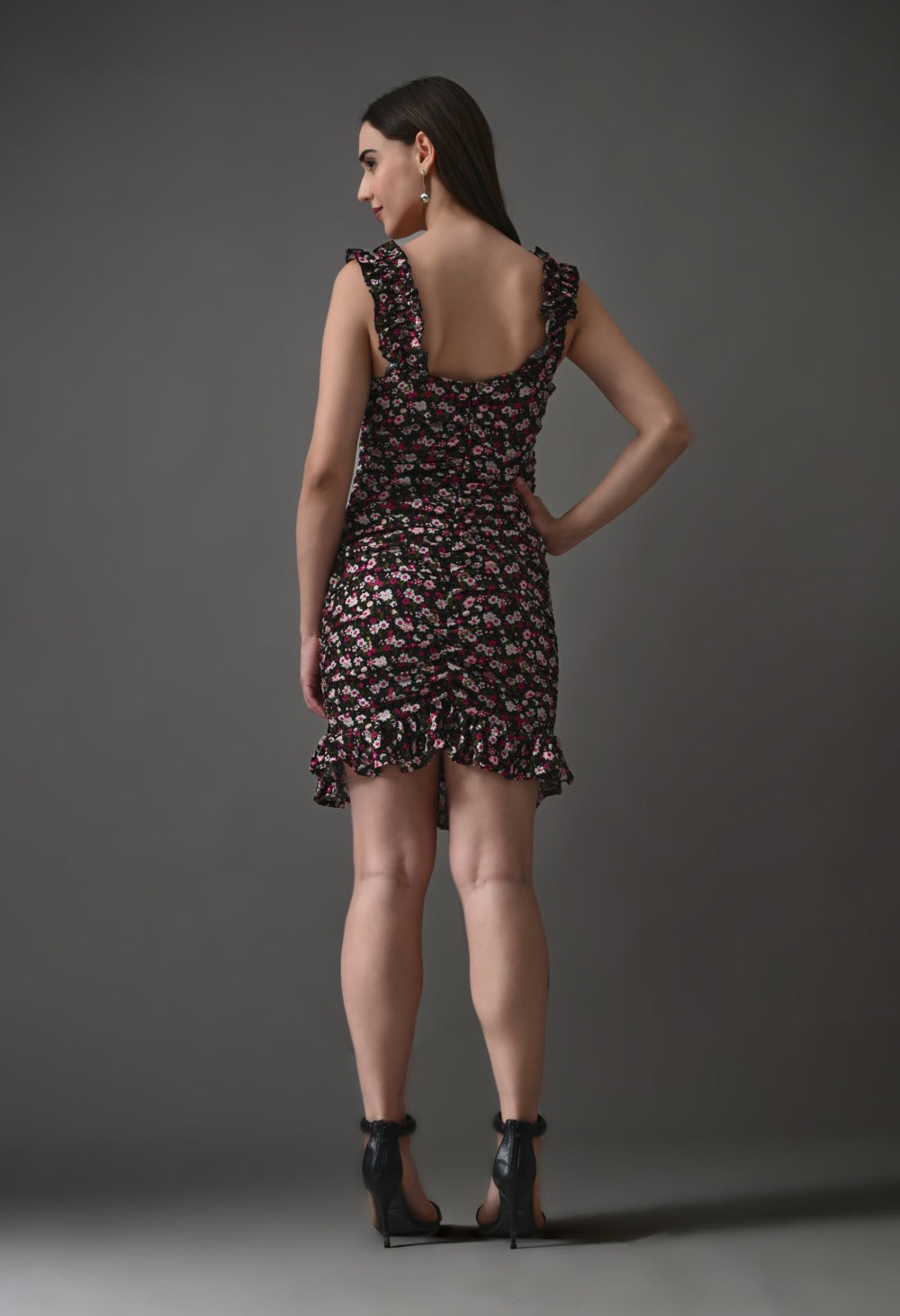 Woman in ruffled floral mini dress and black heels posing against gray background