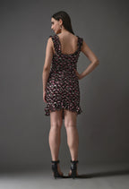 Woman in ruffled floral mini dress and black heels posing against gray background