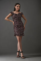 Woman wearing off-shoulder black mini dress with pink floral print and ruffle hem