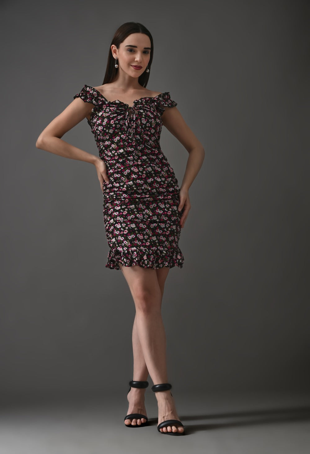 Woman wearing off-shoulder black mini dress with pink floral print and ruffle hem