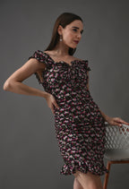 Woman modeling a black floral ruffle dress with pink and white flowers against a gray background