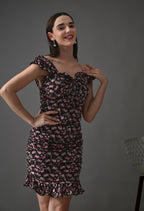 Smiling woman in a ruffled, fitted black floral dress with pink and white flowers